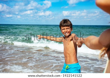 Happy boy pulling mother's hand running to the sea pointing finger