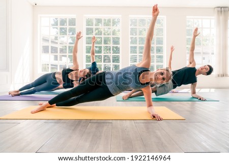 Multi ethnic group of people (Asian, Caucasian) practice yoga together in studio room. Caucasian woman instructor lead side plank pose. Concept of diversity and healthy lifestyles. Royalty-Free Stock Photo #1922146964