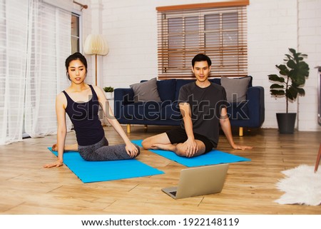Yoga at home concept : Handsome and beautiful asian couple meditate and practice yoga on their laptop, calm their minds on a yoga mat in the living room.