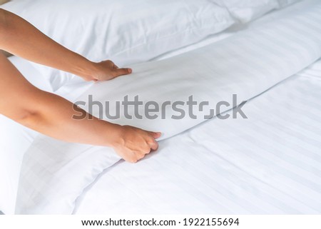 Close up of a female chambermaid hands set up white bed sheet in hotel room, copy space for text