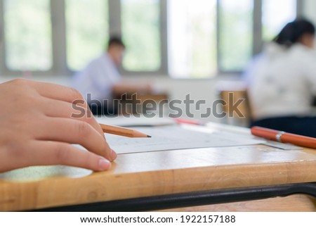 High school or university student reading 
question exam test and using pencil writing on paper answer sheet, lecture chair doing final exam attending in examination classroom with student in uniform Royalty-Free Stock Photo #1922157188