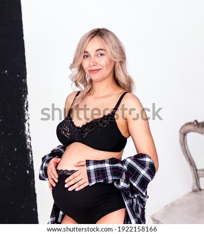 Beautiful pregnant blonde woman in underwear at a photo session in the studio with equipment for high-quality and beautiful pictures.