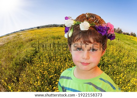 Adorable little boy in a flower wreath at the edge of the field. Birthday today. Israel. Negev desert. Fields of flowers in the bright southern sun. Lovely warm day
