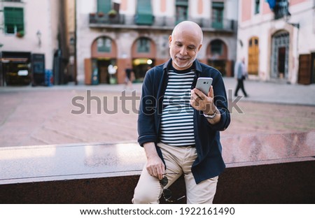 Caucasian retired tourist reading web article with travel advices using modern cellphone gadget at street, aged man connecting to 4g wireless for chatting and booking during international vacations
