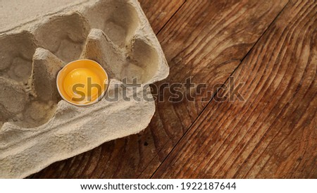One broken egg in a cardboard egg tray. Half egg with yolk in an empty box on wooden background