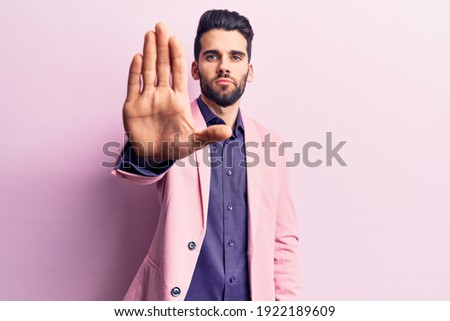 Young handsome man with beard wearing elegant jacket doing stop sing with palm of the hand. warning expression with negative and serious gesture on the face. 