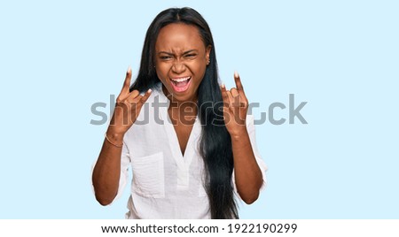 Young black woman wearing casual clothes shouting with crazy expression doing rock symbol with hands up. music star. heavy concept. 