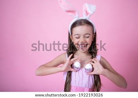 Little girl with easter bunny ears posing holding festive easter eggs in her hands on pink studio background close up.