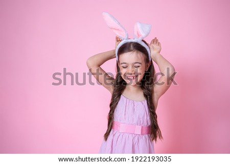 Little girl with Easter bunny ears posing on a studio pink background copy space. Easter holiday concept.
