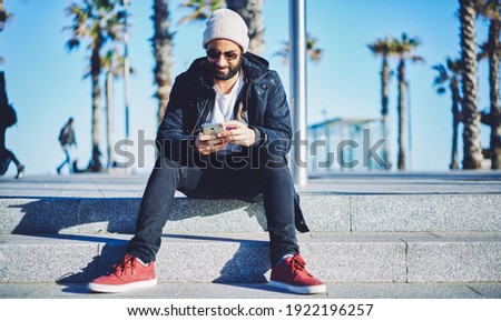 Middle Eastern blogger connecting to 4g wireless for sharing travel publication via mobile application, millennial bearded man chatting via smartphone technology searching web app for installing