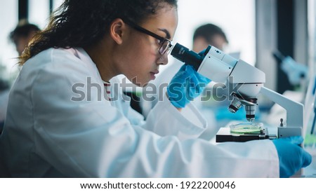 Medical Science Laboratory: Beautiful Black Scientist Looking Under Microscope Does Analysis of Test Sample. Diverse Team of Young Specialists, Using Advanced Technology Equipment. Royalty-Free Stock Photo #1922200046