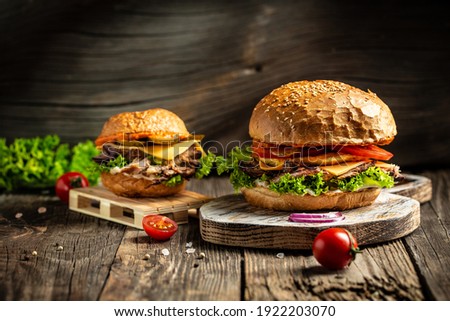 Tasty grilled homemade burgers with beef, tomato, cheese, bacon and lettuce on rustic wooden background. fast food and junk food concept. Royalty-Free Stock Photo #1922203070
