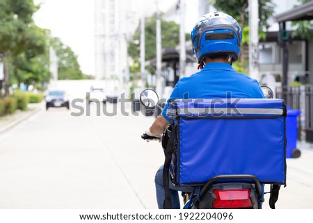 Delivery man wearing blue uniform riding motorcycle and delivery box. Motorbike delivering food or parcel express service Royalty-Free Stock Photo #1922204096