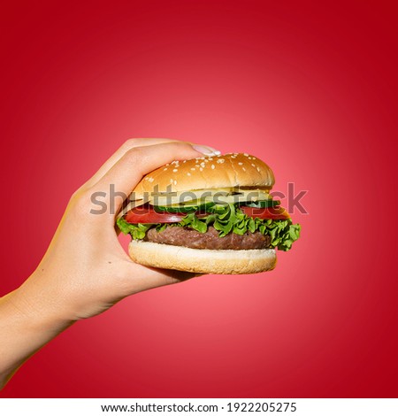 Hand holding a burger in a hot red background. Eating and healthy concept, restaurant food concept. Royalty-Free Stock Photo #1922205275