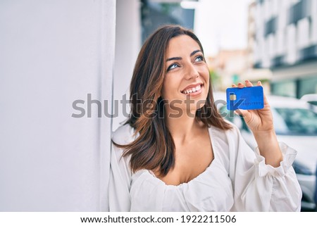 Young hispanic woman smiling happy holding credit card at the city.