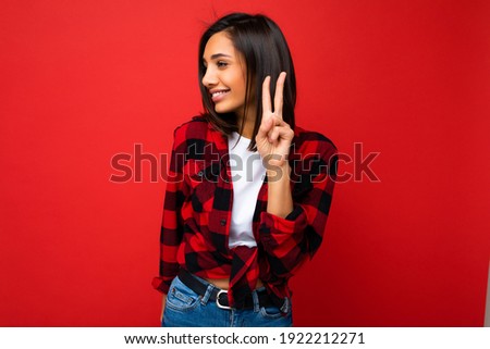 Photo of young positive happy smiling beautiful woman with sincere emotions wearing stylish clothes isolated over background with copy space and showing peace gesture