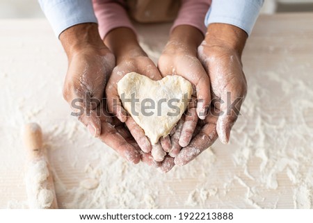 Love And Care Concept. Closeup above top view of unrecognizable african american man and girl baking cake in the kitchen and holding dough in heart shape in hands, dad and daughter cooking together Royalty-Free Stock Photo #1922213888