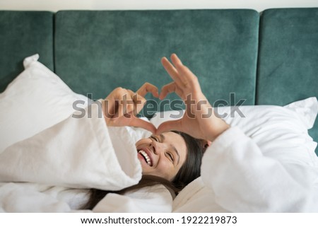 Cropped view of the woman wearing white bathrobe laying in the bed together with her husband and making shape of the heart from their hands. Stock photo