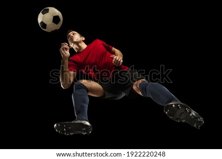 Young caucasian football, soccer player in action, motion isolated on black background, look from the bottom. Concept of sport, movement, energy and dynamic, healthy lifestyle. Training, practicing.
