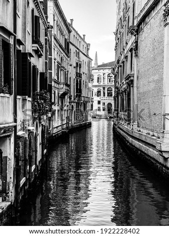 Black and wall picture of a small canal in Venice, Italy, with balcony, and, blue sky reflexion on water, no boat, no people