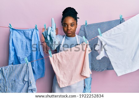 African american woman with braided hair washing clothes at clothesline pointing with finger up and angry expression, showing no gesture 