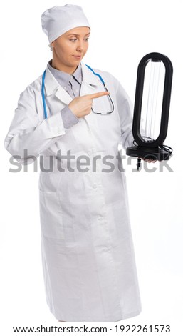 female doctor in a white coat and hat. a medic holds an ultraviolet lamp, points at it, smiles and looks at the lamp. white background, isolated