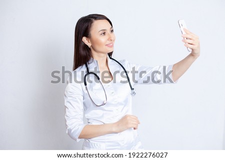 A young beautiful doctor girl takes a selfie and smiles. The doctor is online. Telemedicine. High quality photo