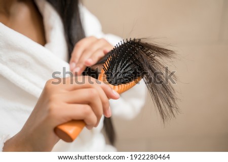 Cropped view of the pretty woman looking at her hair tips and worries about split hair, while brushing her brunette hair at home. Brushing hair concept. Stock photo