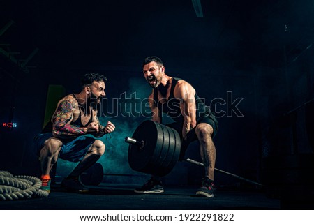 Two muscular bearded tattoed athletes training, one lift heavy weight bar when other is motivating. Scream. Working hard. Exercise for the muscles of the back Royalty-Free Stock Photo #1922291822