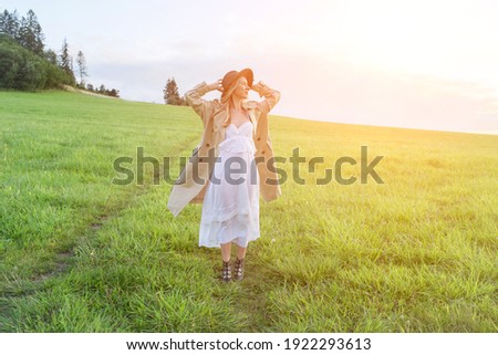 Happy woman enjoying sunset stay on the green grass on the forest peak of mountain. Fresh air, Travel, Summer, Holidays. Health care, authenticity, sense of balance and calmness.