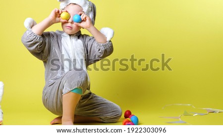 little smiling boy in grey bunny costume covering his eyes with colorful easter eggs. Kids has fun on Easter egg hunt, celebration, selective focus