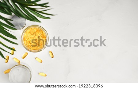 Fish oil capsules with omega 3 and vitamin D in a glass jar on a white concrete table top view, healthy eating concept. Cod liver oil softgels, layout with copy space