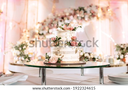 The wedding cake. White, two-tiered, decorated with flowers and gold. On a delicate pink background. Side view, top. Royalty-Free Stock Photo #1922324615