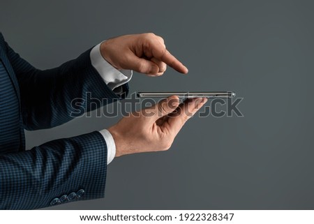 Hands of a businessman in a business suit holds a smartphone horizontally side view and presses the screen with his finger. Close-up