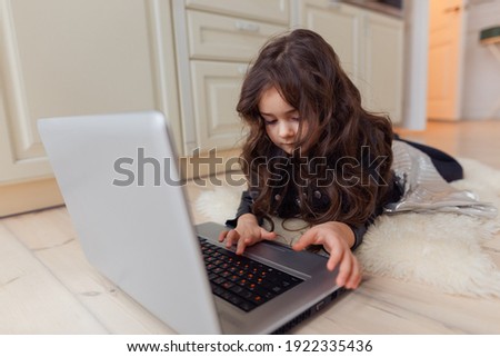 Small cute brunette caucasian baby laying on floor on light artificial animal skin and watching cartoons on laptop with great interest.