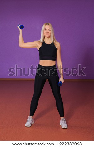 Young blonde woman working out with dumbbells at the gym