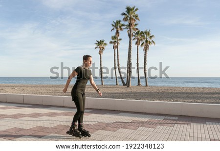 Beautiful fit woman roller skating in promenade at the seaside with palm trees on background.Sport and fitness lifestyle concept with copy space