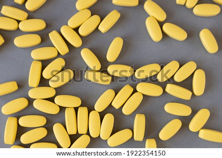 Lots of yellow long vitamins or pills on gray background, close-up, top view. Nutritional supplements concept, health, vitamins, trendy colors of 2021, Illuminating, Ultimate Gray. Flat lay.