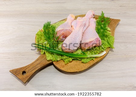 Raw chicken legs. Legs-shaped chicken meat. Chicken meat contains a lot of protein. Legs are laid out on a board, greens, dill, cabbage.