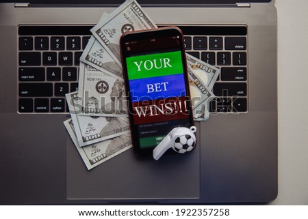 Smartphone with online betting application, dollar bills and soccer ball on a laptop. Gambling concept Royalty-Free Stock Photo #1922357258