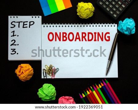 Onboarding symbol. White note with a word 'onboarding' on beautiful black background, colored paper, colored pencils, paper clips, coins and calculator. Business and onboarding concept.