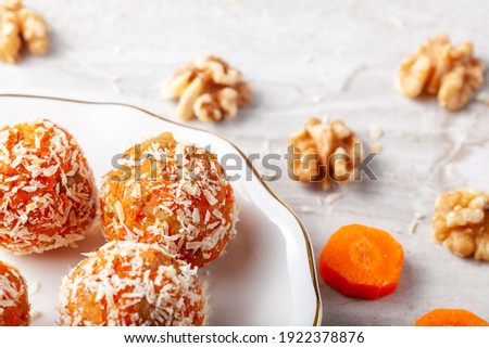 A kitchen countertop with a flat porcelain plate. Homemade fresh carrot bliss balls (mixture of cookie crumbles, walnut and carrot puree) coated with coconut shred are served on the plate. Royalty-Free Stock Photo #1922378876