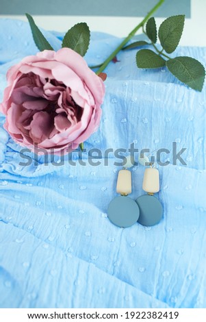 Beautiful earrings with bloom rose on blue cloth background.