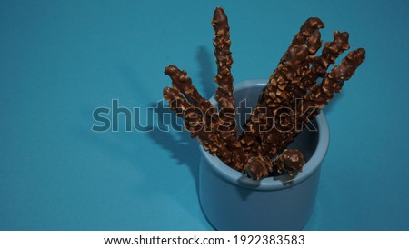 Crispy sticks with hazelnut sprinkles in chocolate on a blue background.