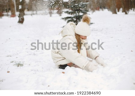 Child in a knited hat. Little girl plays with snow.