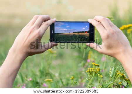Holding smart phone with two hands horizontally and taking photos of summer wheat field summer sunny nature landscape