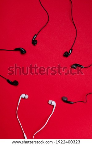 Vertical image of many earphones on the red surface.Empty space.Concept of trendy audio chats and Clubhouse app