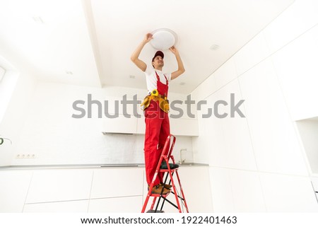 Electrician at work. Service for the repair of electrical wiring and replacement of ceiling lamps. A builder is installing a loft-style wooden ceiling. Rent-a-gent helps with the housework Royalty-Free Stock Photo #1922401463
