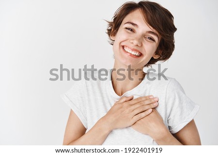 Close up of happy smiling woman say thank you, holding hands on heart grateful, express gratitude, standing against white background. Royalty-Free Stock Photo #1922401919