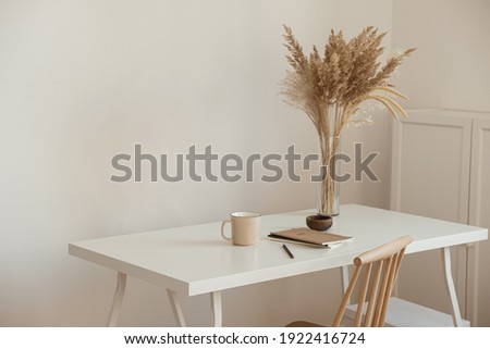 Aesthetic minimal office workspace interior design. Mug, notebook, pampas grass floral bouquet on white table against white wall. Girl, woman boss work at home business concept. Royalty-Free Stock Photo #1922416724